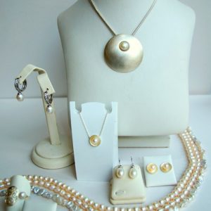 Elegantes Perlen-Schmuckset mit großem Anhänger, passenden Ohrringen, Ringen und mehreren Perlenketten, präsentiert auf weißen Schmuckdisplays.