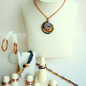 Präsentation eines Schmucksets in Gold und Roségold: Kette mit rundem Anhänger, passende Ringe, Armband und Creolen, arrangiert auf weißen Ständern.