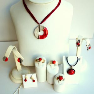 Schmuckarrangement mit roten Stein-Elementen, bestehend aus Halsketten, Ohrringen, Ringen und einem Armband, auf weißen Ständern präsentiert.