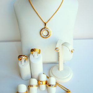 Goldfarbenes Schmuckset mit funkelnden weißen Steinen: eine runde Anhängerkette, Ohrstecker, mehrere Ringe sowie ein zweiter runder Anhänger mit filigranem Baummotiv